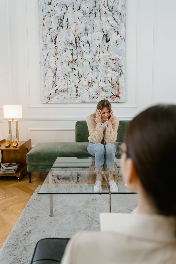 A distressed woman sitting on a green sofa during a therapy session indoors.