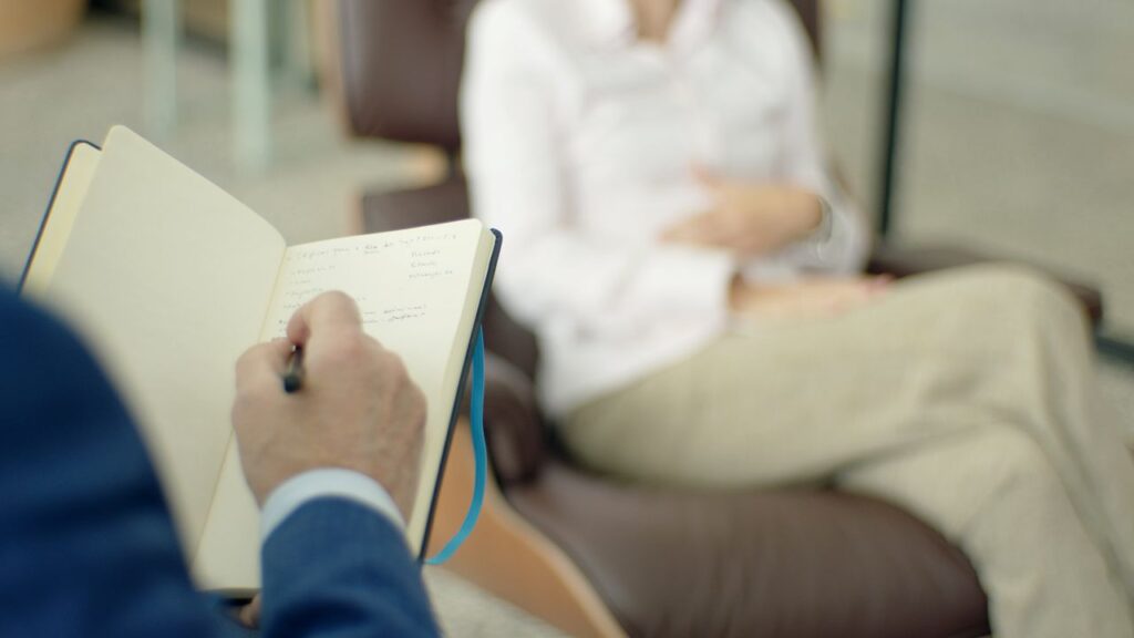 Therapist writing notes during a counseling session with a client.